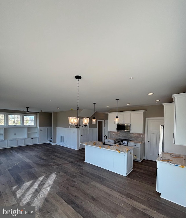 kitchen with white cabinets, a sink, stainless steel appliances, a center island with sink, and backsplash