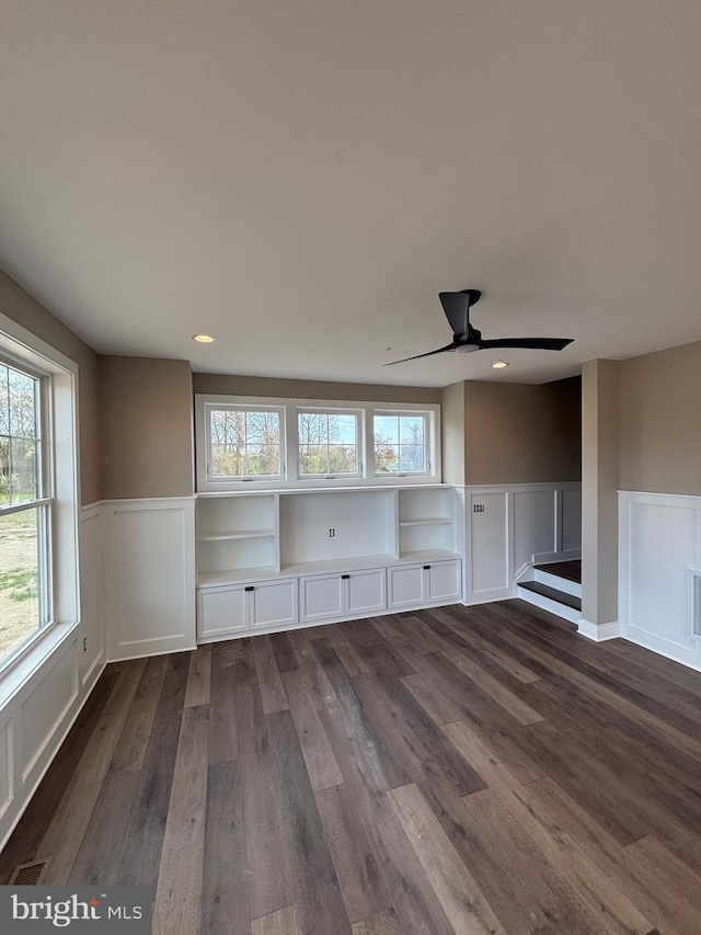 unfurnished living room featuring a decorative wall, a wainscoted wall, a ceiling fan, and dark wood-style floors