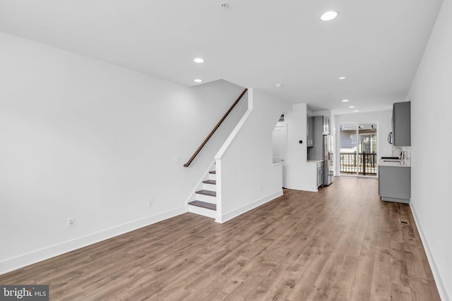 unfurnished living room featuring recessed lighting, light wood-style flooring, baseboards, and stairs