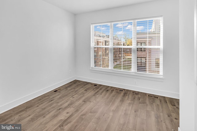 spare room with plenty of natural light, visible vents, baseboards, and wood finished floors