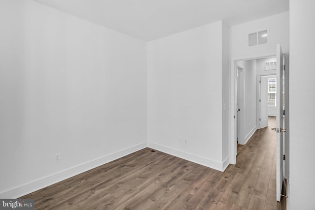 empty room with dark wood-style flooring, baseboards, and visible vents