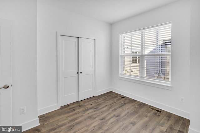 unfurnished bedroom featuring a closet, visible vents, dark wood-style flooring, and baseboards