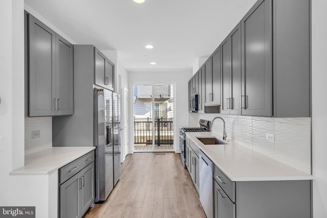 kitchen with a sink, light countertops, stainless steel appliances, gray cabinets, and backsplash