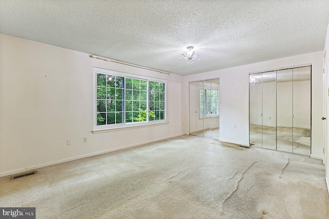 unfurnished bedroom with multiple closets, carpet flooring, baseboards, and a textured ceiling