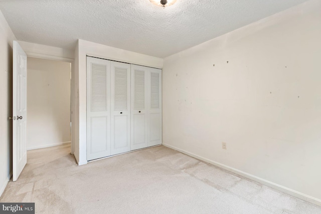 unfurnished bedroom with light colored carpet, a closet, baseboards, and a textured ceiling