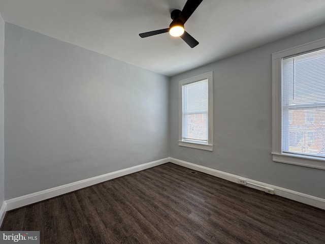 empty room featuring baseboards, dark wood-style flooring, ceiling fan, and a wealth of natural light