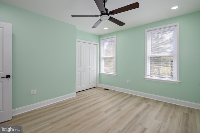 unfurnished bedroom with a closet, baseboards, multiple windows, and wood finished floors