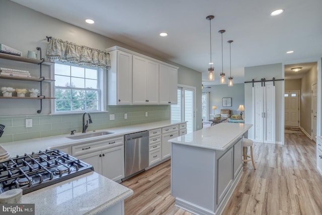 kitchen featuring stainless steel dishwasher, white cabinetry, a barn door, a center island, and a sink