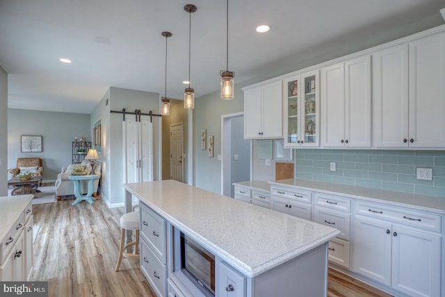 kitchen featuring a barn door, stainless steel microwave, light wood-type flooring, decorative backsplash, and white cabinetry