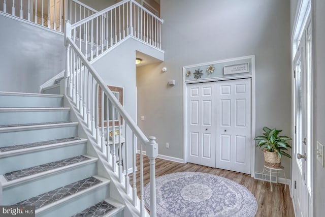 foyer entrance featuring baseboards, wood finished floors, a high ceiling, and stairway