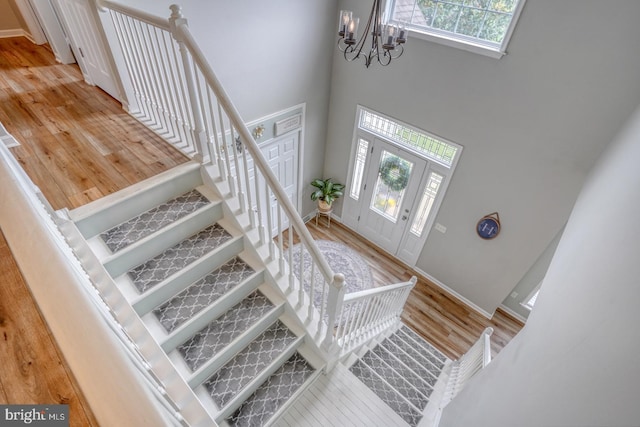foyer entrance featuring baseboards, an inviting chandelier, wood finished floors, a high ceiling, and stairway
