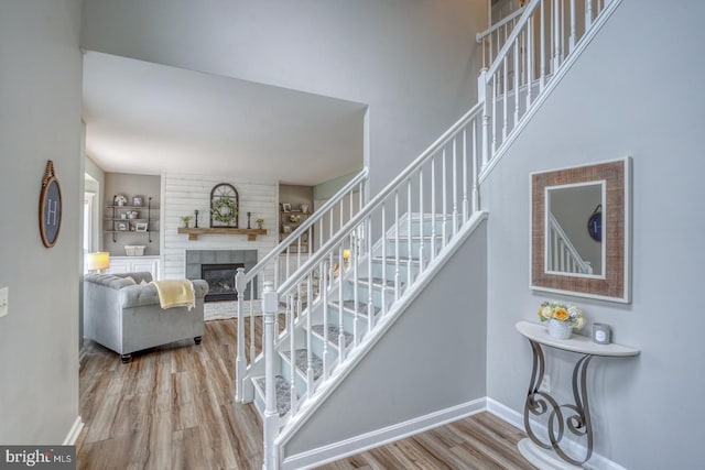 stairway with wood finished floors, baseboards, and a large fireplace
