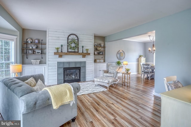 living room with built in shelves, baseboards, a chandelier, wood finished floors, and a large fireplace