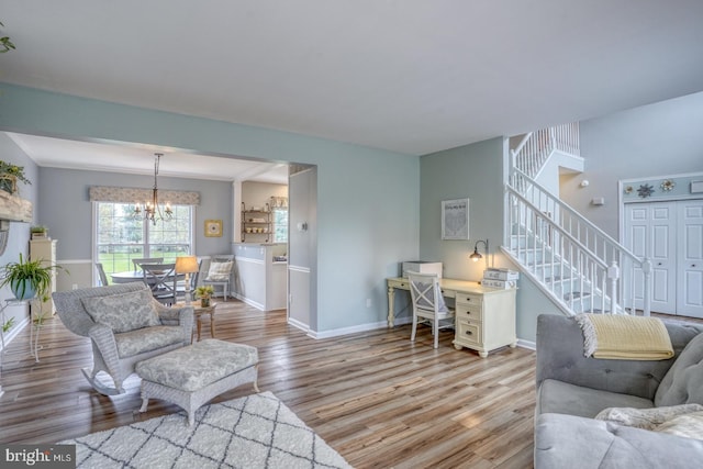living area featuring baseboards, light wood finished floors, a notable chandelier, and stairs