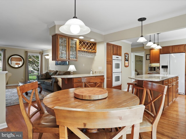 dining area featuring indoor bar, light wood-style floors, crown molding, and baseboards