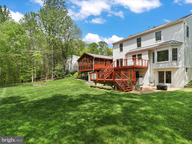 rear view of property featuring a lawn, a patio, a wooden deck, a sunroom, and stairs