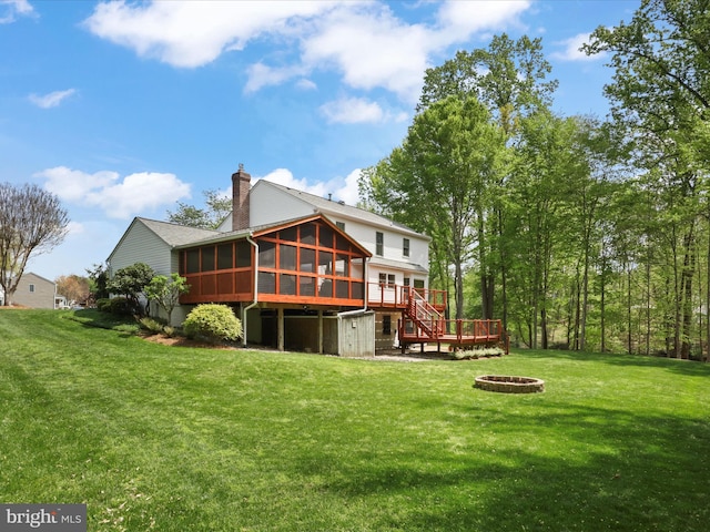 rear view of house featuring a chimney, a wooden deck, a lawn, a fire pit, and a sunroom