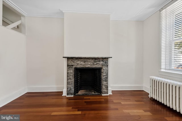 unfurnished living room with crown molding, radiator, wood finished floors, and a wealth of natural light