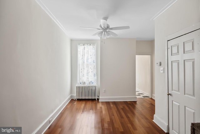 empty room with wood finished floors, ornamental molding, radiator, and ceiling fan