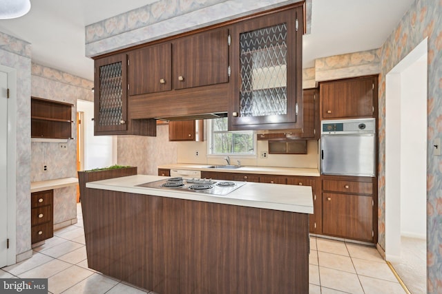 kitchen with a sink, stainless steel oven, electric stovetop, light countertops, and light tile patterned floors