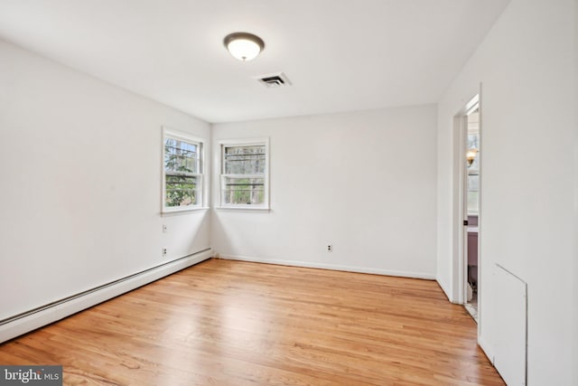 spare room with a baseboard heating unit, visible vents, light wood finished floors, and baseboards