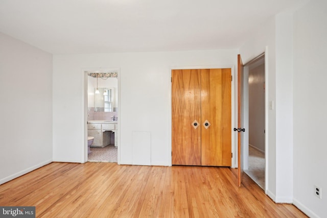 unfurnished bedroom featuring a sink, connected bathroom, light wood-style floors, a closet, and baseboards