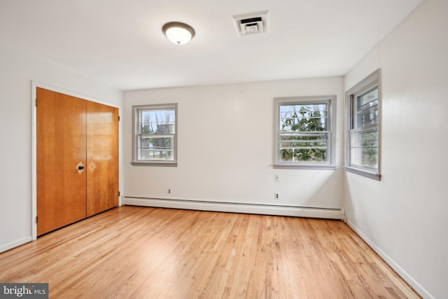 unfurnished bedroom featuring a baseboard radiator, light wood-style flooring, visible vents, and multiple windows
