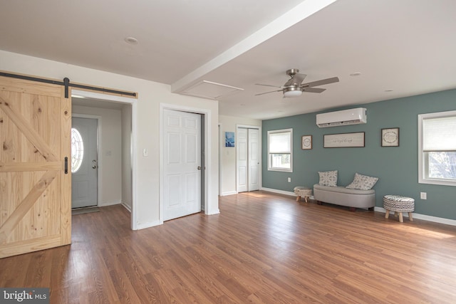 sitting room with a wall unit AC, ceiling fan, wood finished floors, and a healthy amount of sunlight