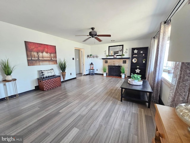living area featuring a brick fireplace, a ceiling fan, and wood finished floors