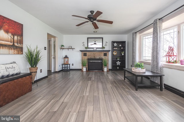living area featuring baseboards, a ceiling fan, wood finished floors, and a brick fireplace