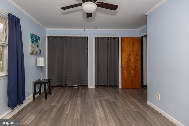 unfurnished bedroom with two closets, wood finished floors, baseboards, and ornamental molding