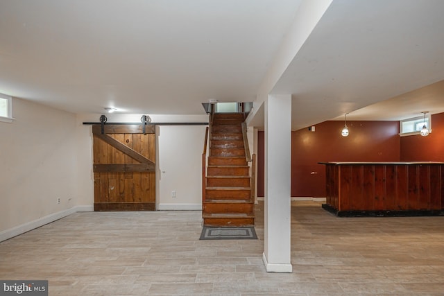 below grade area featuring a barn door, a bar, a wealth of natural light, stairway, and wood finished floors