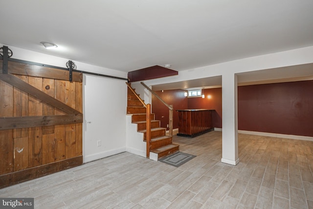 below grade area featuring indoor bar, baseboards, a barn door, light wood-type flooring, and stairs