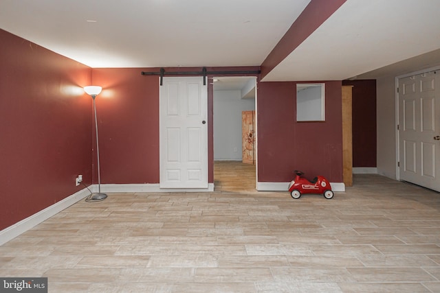finished below grade area with a barn door, light wood-style floors, and baseboards