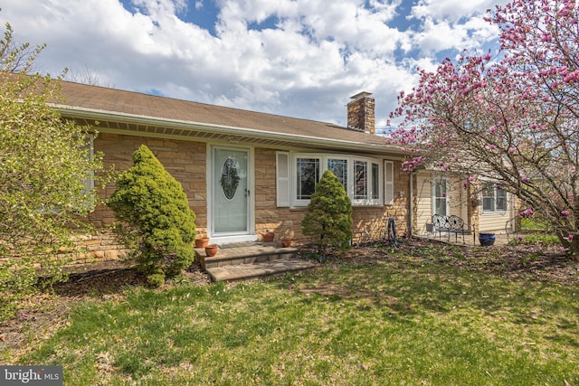 ranch-style home featuring a front yard, stone siding, and a chimney