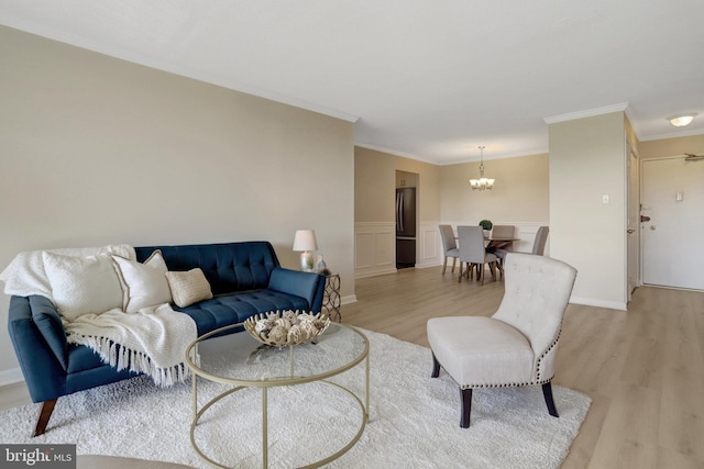 living room featuring wainscoting, an inviting chandelier, ornamental molding, and light wood finished floors