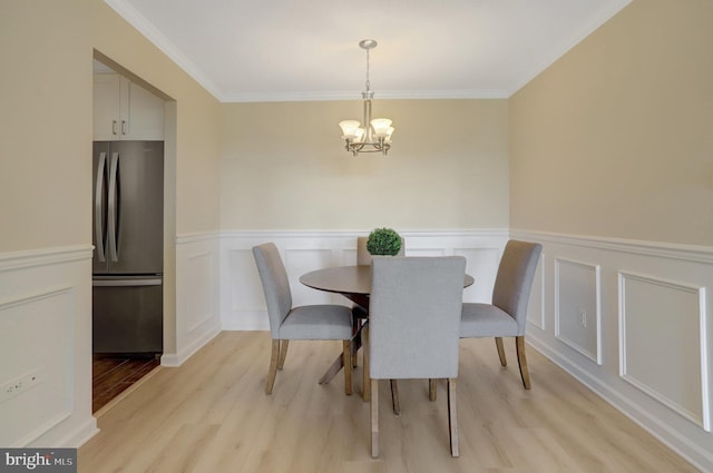 dining room featuring an inviting chandelier, ornamental molding, wainscoting, a decorative wall, and light wood-style floors