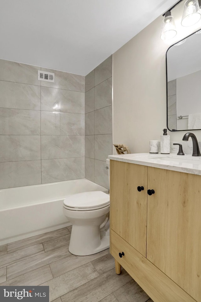 bathroom featuring a washtub, visible vents, wood finished floors, vanity, and toilet