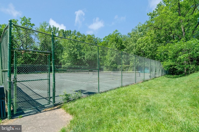 view of tennis court with a lawn, a gate, and fence
