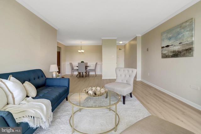 living area with baseboards, a notable chandelier, ornamental molding, and light wood-style floors