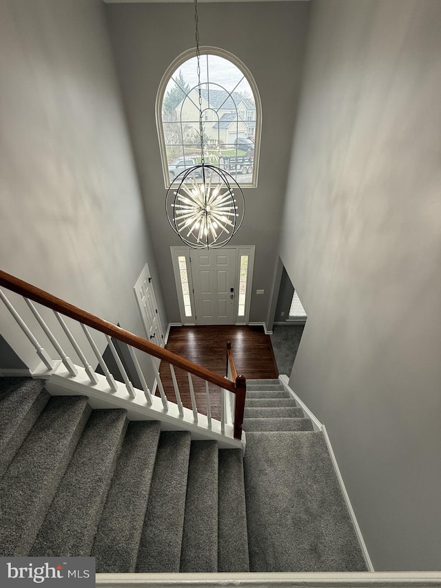 stairway with baseboards, wood finished floors, a notable chandelier, and a towering ceiling