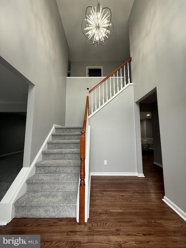stairs with baseboards, an inviting chandelier, a high ceiling, and wood finished floors