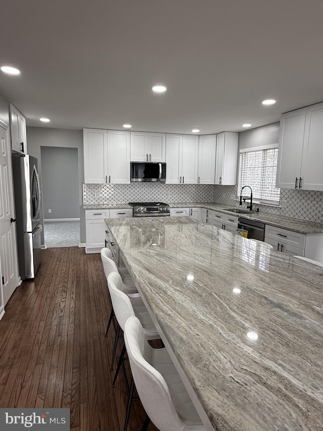 kitchen featuring white cabinets, a sink, dark wood finished floors, stainless steel appliances, and light stone counters