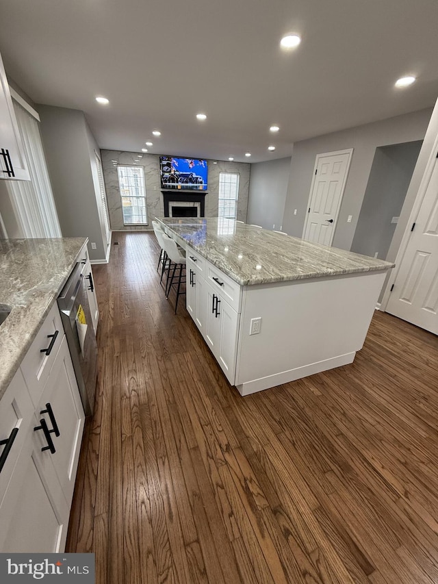 kitchen with a fireplace, open floor plan, a kitchen island, white cabinets, and dark wood finished floors