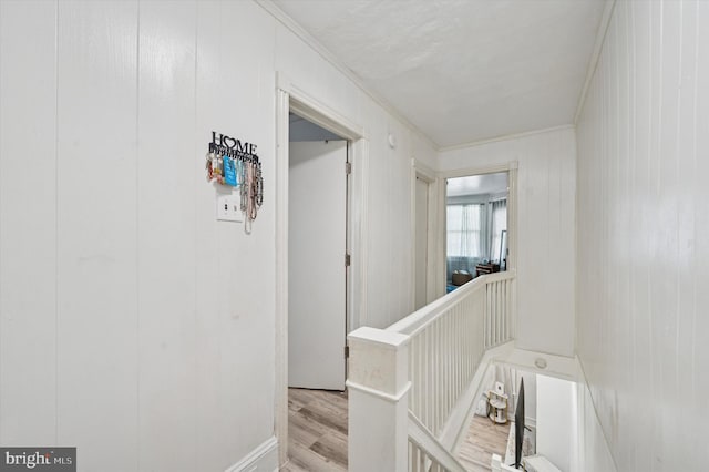 hallway with light wood-style floors, ornamental molding, and an upstairs landing