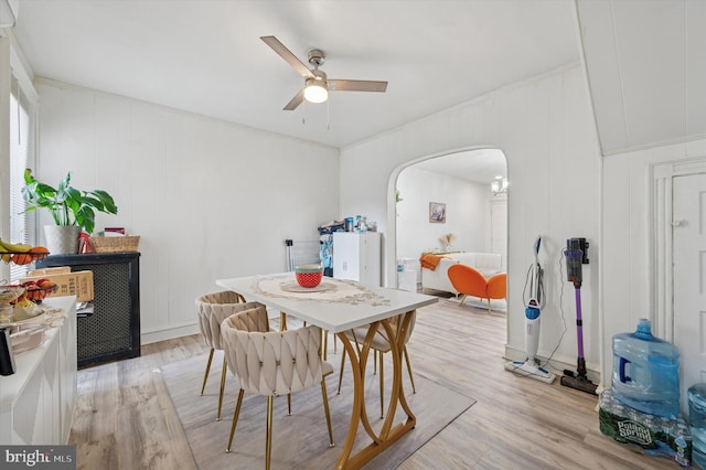 dining room featuring arched walkways, ceiling fan, a decorative wall, and light wood-style flooring