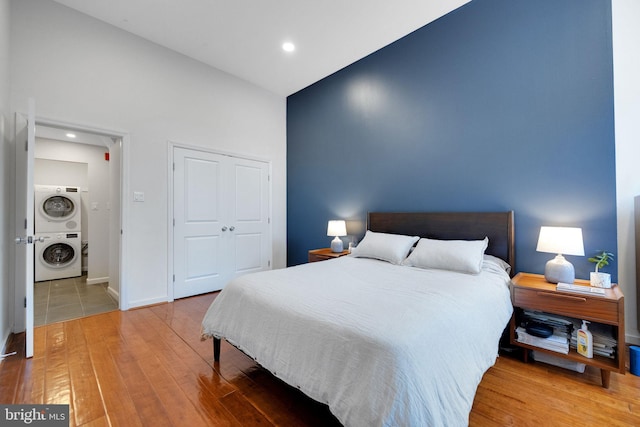 bedroom with wood finished floors, stacked washing maching and dryer, baseboards, a closet, and recessed lighting