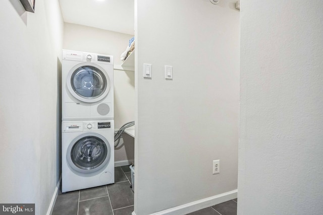 laundry area with baseboards, stacked washer and dryer, laundry area, and dark tile patterned floors