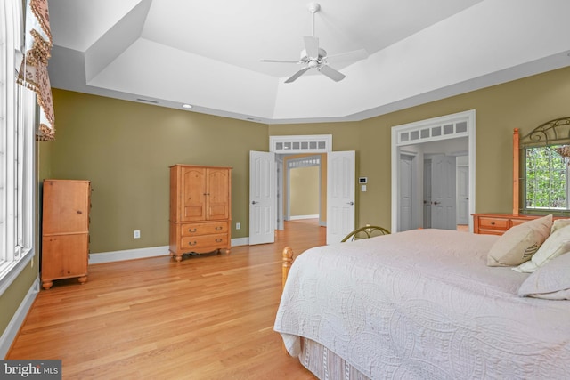 bedroom featuring a ceiling fan, light wood-type flooring, a tray ceiling, baseboards, and visible vents