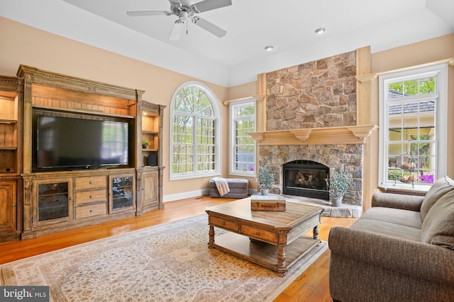 living room with vaulted ceiling, a stone fireplace, a ceiling fan, and wood finished floors